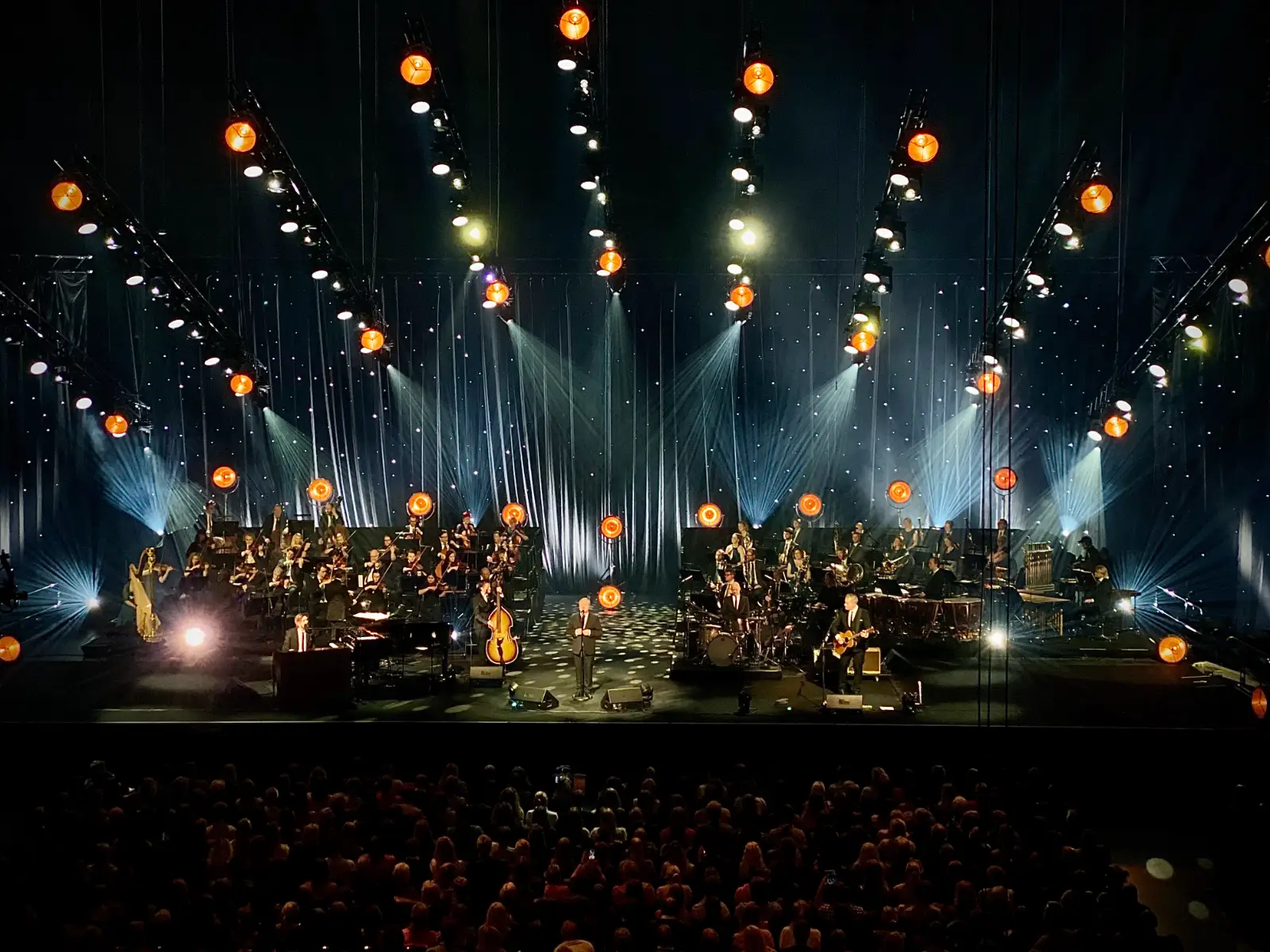 Stor konsertscene med orkester og band, dramatisk scenelys og fullsatt publikum